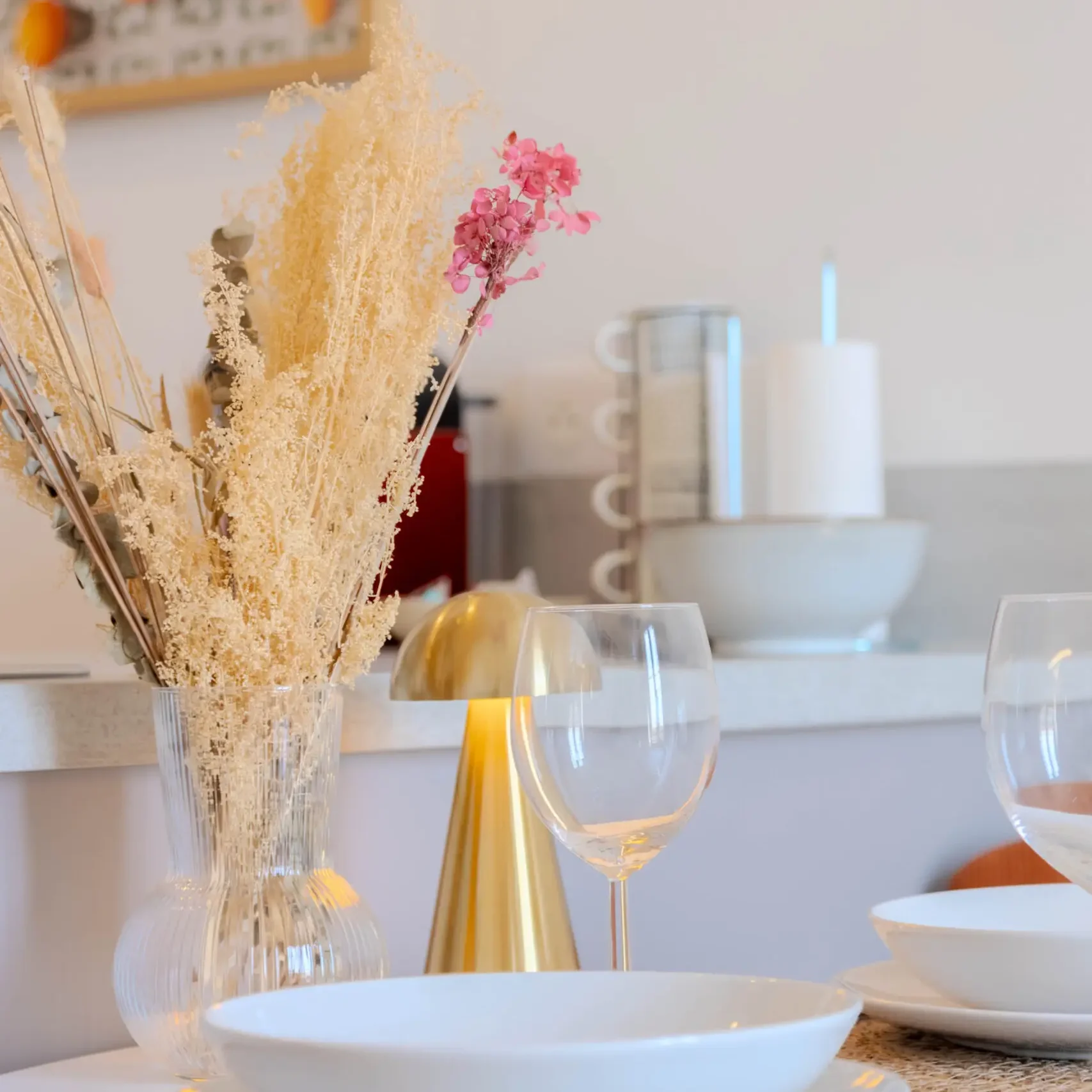 Ambiance chaleureuse avec bouquet de fleurs séchées et verres prêts pour un apéritif à la maison.