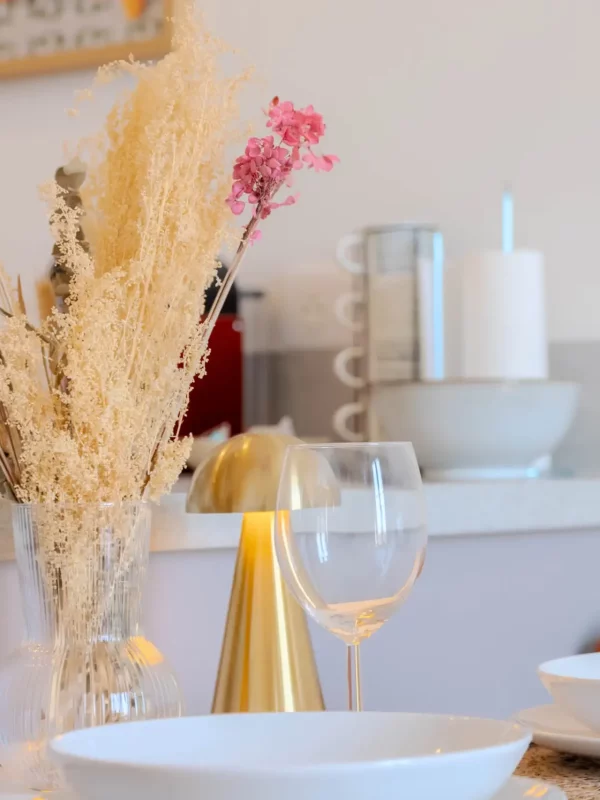 Ambiance chaleureuse avec bouquet de fleurs séchées et verres prêts pour un apéritif à la maison.